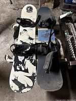 Top view showing two snowboards with attached bindings, clear graphic on one with silhouette design, and showing wear.