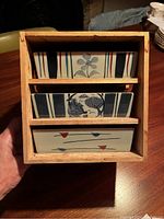 Top-down view of three square ceramic dishes nested in a wooden box, showing their unique designs and box condition.