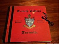 Red cover of the commemorative folio titled 'Trinity College Toronto' with black binding and a black ribbon tie.