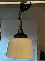 Photo of vintage milk glass pendant light hanging, showing large white glass shade and dark brass painted holder with chain