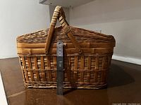 Side view of vintage wicker picnic basket with handles upright. A ruler is placed in front showing about 12 inches height.