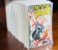 Stack of comic books in protective sleeves showing Moon Knight #26 front cover with notebook-style background