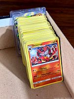 Large stack of Pokémon cards shown in a box, featuring an Incineroar card as the topmost card.