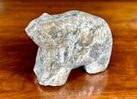 Front angled view of gray mottled stone bear sculpture on polished wood surface
