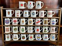 Full view of three-tier wooden shelf holding approximately 30 white porcelain tankards with various brewery logos and advertisements.