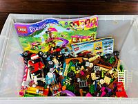 Overview of the plastic bin containing mixed LEGO pieces, instruction booklets visible at the back including LEGO Friends 41034