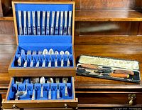 Full view of the Oneida Community Coronation pattern flatware set in blue velvet-lined wooden chest with two drawers, alongside separate carving set in case.