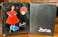 Two vintage Barbie doll cases side by side, one with artwork of Barbie in a red dress and the other black with white polka dots and pink Barbie logo.