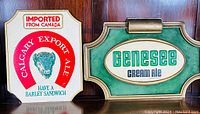 Both Calgary Export Ale and Genesee Cream Ale plastic beer advertising signs displayed side by side on a shelf.