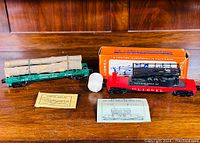 Two Lionel O gauge train cars displayed on a wooden surface. Includes Track Maintenance Car 6912 in red and black with original box and paperwork, and a green log car 6361 with real wooden logs chained on top plus original paperwork.