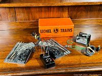 Wide photo showing all items in the lot arranged on a wooden surface, including two track switches, the transformer, wired remote control, wiring accessories, and original Lionel box.