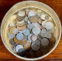Top-down view of a tin filled with assorted world coins, showing a mix of silver and base metal coins in circulated condition.