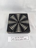 Top view of closed black square puzzle box with white geometric pattern, signs of wear.