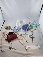 Photo showing 8 rosaries in various colors and conditions, including some in organza bags and some loose with metal crucifixes.