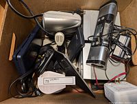 Box filled with multiple electronic items and accessories including speakers, joysticks, chargers, and other devices.