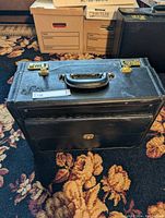 Photo of the black hardbody briefcase with gold-colored locks, handle on top, and front pocket.