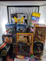 Multiple Pokemon tins and boxes arranged in display: lunchbox, 2 Umbreon tins, gold and mini tins, display boxes