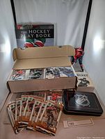 Photo showing box of hockey cards in binder sleeves, two hockey books and collectible figurine, plus NHL tin and some loose sealed card packs
