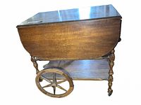 Side view showing solid wood construction, one drop leaf extended, large spoked wheel and turned legs.