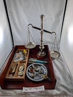 Photo showing the entire lot of a vintage metal balance scale with wooden base, wooden letter tray with compartments holding souvenir spoons, small collectibles, and some pens, all displayed on a wooden tray.