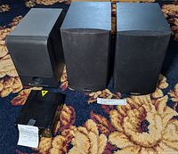 Three speakers including two Paradigm speakers and one Altec Lansing speaker, placed on a carpeted floor along with a black red & green laser light unit.