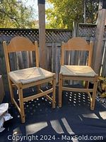 Two wooden chairs with woven rush seats placed outdoors showing front and side views.
