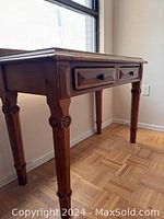 Side and front corner angle displaying carved legs and two drawers with wood knobs.