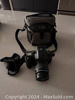 Canon EOS Elan 7N camera with attached 28-105mm lens and Canon branded camera strap, positioned on counter next to carrying bag.