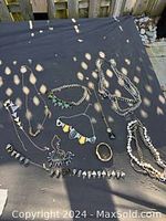 Overview photo of various pieces of costume jewelry laid out on black fabric, includes several necklaces, bracelets, and earrings.