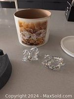 Two Swarovski crystal swan figurines displayed on a table beside floral decorated round box and lid