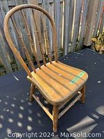 Photo showing front and side view of antique child's chair with curved spindle back and worn natural wood finish.