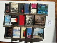 Photo showing 16 Rush CDs in jewel cases with visible front covers, arranged in three rows on a white background.