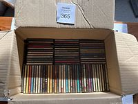 Two open cardboard boxes filled with assorted CDs arranged in rows showing spine labels and titles.