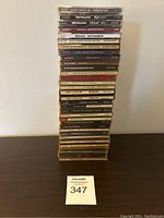 Vertical stack of 31 metal and rock CDs on a dark wood surface against white wall showing album spines for Metallica, Black Sabbath, Queen, Scorpions and others.