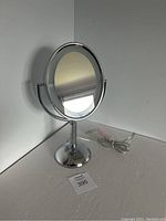 Oval mirror mounted on chrome stand with power cord, front view without light on.