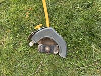Close-up of the Ryobi edger blade and gray protective guard with yellow attachment arm handle