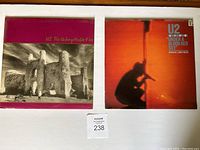 Front covers of U2 albums 'The Unforgettable Fire' and 'Under a Blood Red Sky' placed side by side on a white surface with a lot number tag below.
