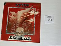 Front cover of ZZ Top vinyl album 'Deguello' showing skull with horn and laser graphics on red background.