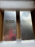 Two sealed silver-tone bricks labeled $500 each inside packing foam