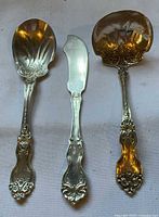 Full view of three Wallace La Reine sterling pieces: serving spoon, butter spreader, gold-washed ladle