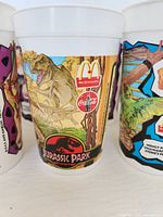 Close up of a Jurassic Park cup showing T-Rex, McDonalds, Coca-Cola logos and colorful design