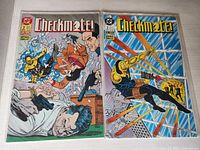 Photo of two vintage comic books from the Checkmate! series, issues #2 and #3, with illustrated colorful covers showing dynamic action scenes.