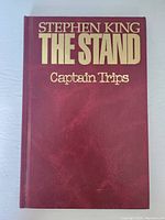 Front cover of the hardcover graphic novel titled 'Stephen King The Stand Captain Trips' showing dark red faux leather texture with gold embossed letters.