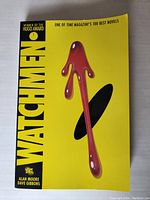 Front cover of the Watchmen graphic novel showing the iconic blood-stained smiley face pin design with yellow background.