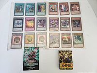 Photo showing 18 distinct Yu-Gi-Oh! trading cards in plastic sleeves alongside a beginner's guide booklet and an official playing card deck box.