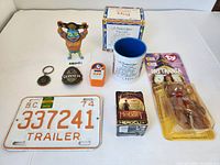 Photo showing 8 assorted collectibles including McDonald's wrestler figure, Guinness and other keychains, Hobbit Heroclix figure, Britannia action figure, mug, and vintage trailer license plate.