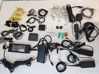 Top view of approximately 35 mixed computer chargers, power adapters, and cables including Dell, Lenovo, HP items plus various USB, power cables, and adapters in black and white.
