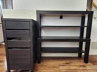 Black filing cabinet on wheels with three small drawers and one large filing drawer, next to two black shelves with two shelf surfaces each.