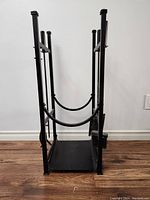 Front view of the black metal fireplace log rack showing curved wood supports and rectangular base