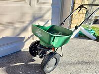 Side view of green Scotts Turf Builder seed spreader showing plastic hopper and wheels.